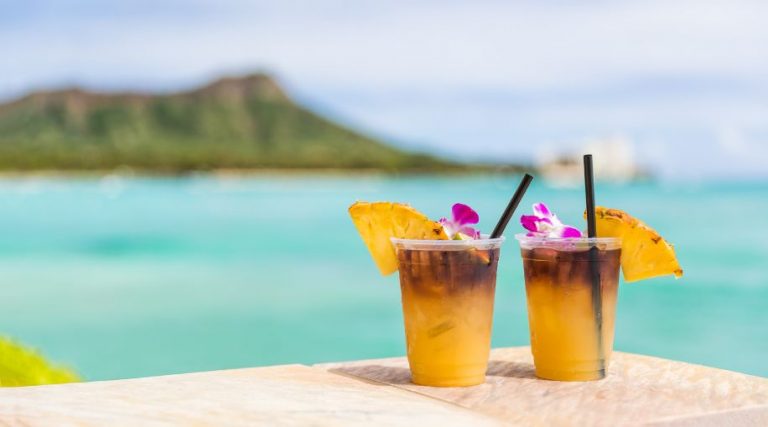 Two fruit cocktail drinks on a table at the beach.