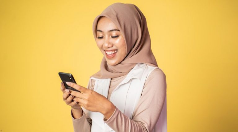 A woman standing against a yellow background using a phone.